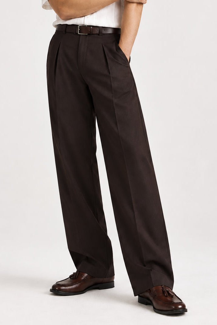 A model wearing dark brown pleated trousers and a white shirt stands against a light gray studio background. Text on the image reads 'EVERYDAY KOREAN FIT', 'PLEATED TROUSER', and 'SHOP NOW'.