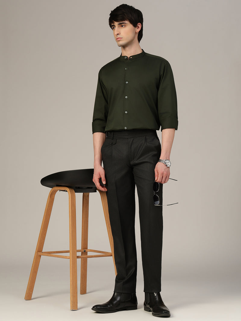 Man wearing a green shirt and black pants standing next to a black stool on a plain background