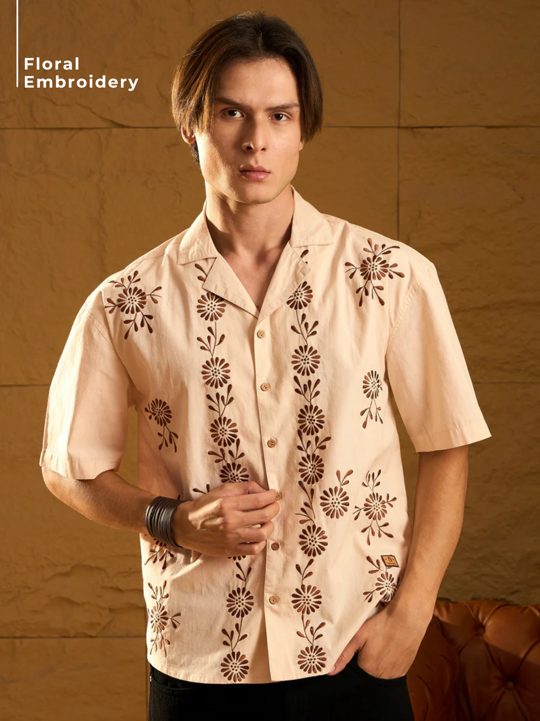 Man wearing a beige shirt with floral embroidery against a brown background