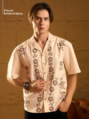 Man wearing a beige shirt with floral embroidery against a brown background