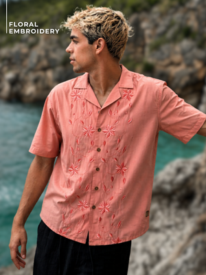 Man wearing a pink floral embroidered shirt by a rocky coastline
