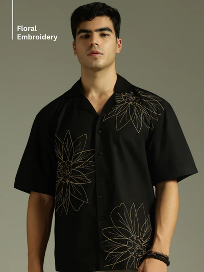 Man wearing a black shirt with floral embroidery on a gray background