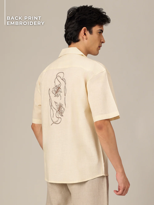 Man wearing a beige shirt with back print embroidery on a plain background