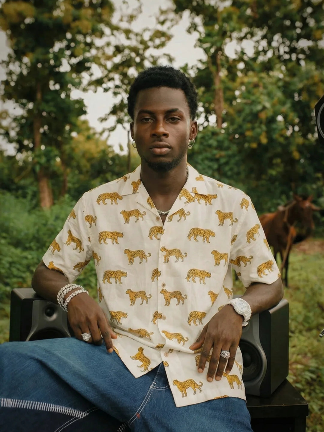 Man wearing a patterned shirt sitting outdoors with trees in the background