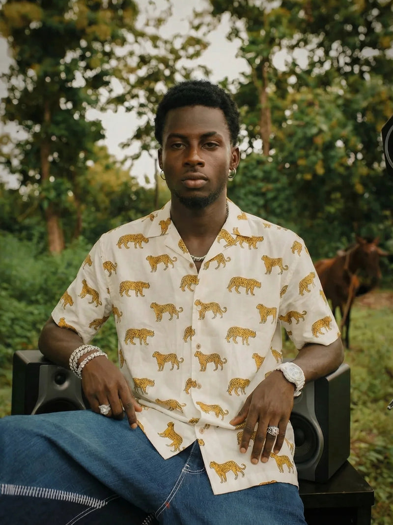 Man wearing a patterned shirt sitting outdoors with trees in the background