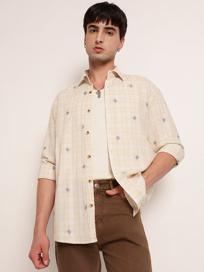 Man wearing a cream checkered shirt and brown pants against a white background