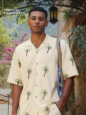 Man wearing a tropical embroidered shirt with palm tree patterns in an outdoor setting.