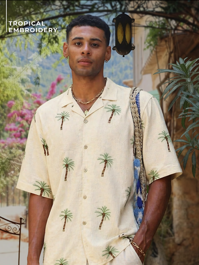 Man wearing a tropical embroidered shirt with palm tree patterns in an outdoor setting.