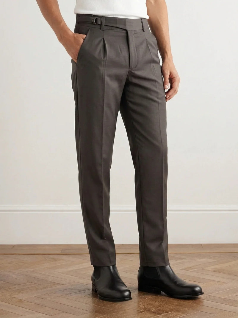 Person wearing brown dress pants and black shoes on a wooden floor.